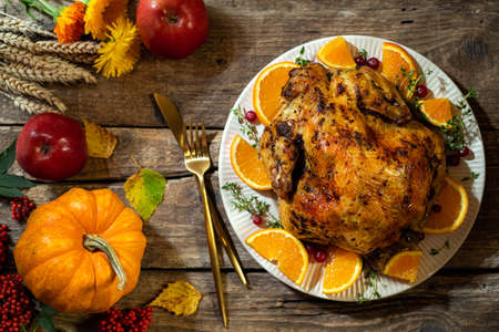Thanksgiving background. Baked chicken or turkey with citrus and spices for celebrations for Thanksgiving Day on wooden table. Autumn table settings for Thanksgiving dinner. Top viewの写真素材