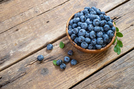 Fresh blueberry in wooden bowl. Juicy and fresh blueberries with green leaves on rustic table. Concept blueberry antioxidant for healthy eating and nutrition. Top view, copy spaceの写真素材