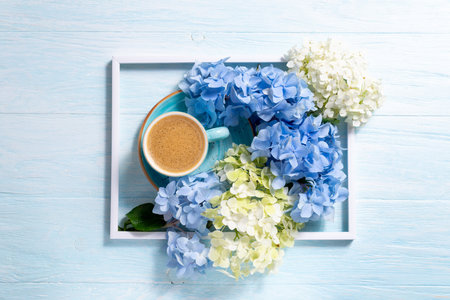 Bouquet of beautiful hydrangea and coffee cup on blue wooden background. Blue flowers hortensia. Abstract floral composition with blue and white flowers. Copy spaceの写真素材