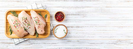 Raw uncooked chicken breasts with spices and herbs on white wooden background, meat with ingredients for cooking. Top view, copy spaceの写真素材