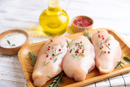 Chicken fillet with herbs and spices on white wooden table close up. Chicken meat with ingredients for cookingの写真素材