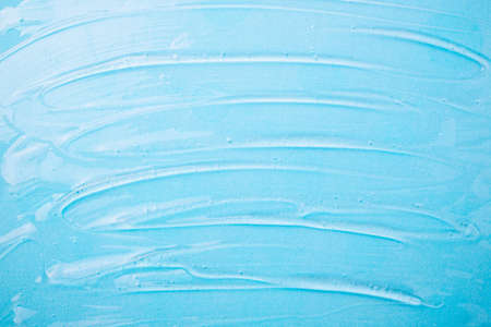 Liquid gel cosmetic on blue. Texture of blue gel or sanitizer. Pattern of transparent gel for face cleansing. Moisturizing cosmetic beauty product for skincare. Lotion or serum cosmetics product for skin careの写真素材