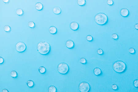 Pattern of transparent drops cosmetics gel for face cleansing. Liquid gel cosmetic on blue. Moisturizing cosmetic beauty product for skincare. Lotion or serum cosmetics product for skin careの写真素材