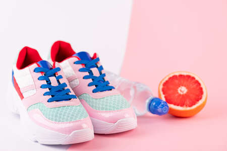 Sport equipment sport shoes, bottle of water, citrus fruits on pink and white background. Healthy lifestyle, fitness, diet, slimming concept. Trendy female sport accessories, copy spaceの写真素材