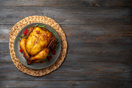 Baked chicken for festive dinner. Cooked chicken or turkey with herb rosemary and berries on wooden table. Thanksgiving holiday concept. Copy spaceの写真素材
