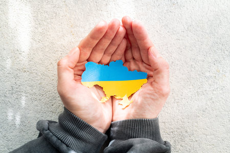 Hands holding the national flag of Ukraine in the shape of the borders of Ukraine. Support for Ukraine in the war with Russia. stop the war conceptの写真素材