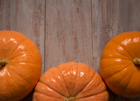 Three beautiful orange pumkins on the wooden boards background.の写真素材