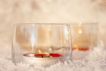 Two red candles in the glasses on the shining snow background.の写真素材