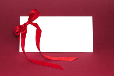 Gift isolated white card with elegant silk red ribbon bow on deep red background. Cut out.の写真素材