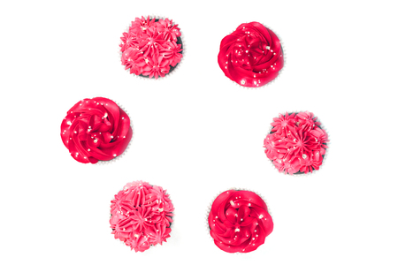Several delicious chocolate cupcakes with red and pink creamy icing on isolated white background arranged in circle. Top view.の写真素材