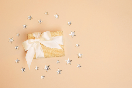 Traditional sparkling golden present box with a satin bow on pastel background decorated with shiny silver stars. Copy space.の写真素材