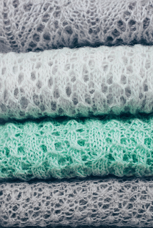 Stylish knitted pastel colored sweaters in different knitting patterns folded in stack. Winter and spring season knitwear clothing with clearly visible texture. Close up, copy space.の写真素材