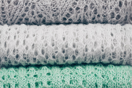 Stylish knitted pastel colored sweaters in different knitting patterns folded in stack. Winter and...