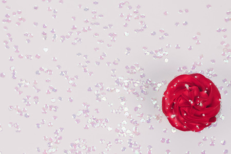 Tempting cupcake with red icing on festive white background sprinkled with pearly confetti. Top view. Copy space.の写真素材