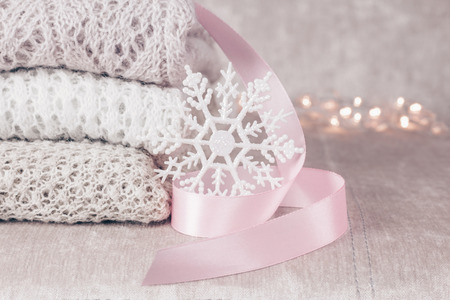 Stylish knitted pastel colored sweaters in different knitting patterns folded in stack with snowflake and pink satin ribbon on velvety fabric background. Close up, copy space.の写真素材