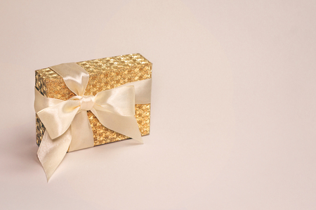 Beautiful shiny golden present box with a silk bow on pastel background. Copy space.の写真素材