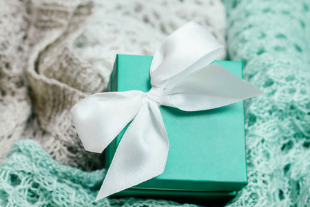 Stylish knitted pastel colored sweaters in different knitting patterns with mint colored present box with white satin bow. Winter and spring season knitwear clothing.の写真素材