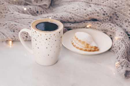 Warm cozy knitwear and a cup of coffee with a cake on white marble windowsill against white window background. Copy space.の写真素材
