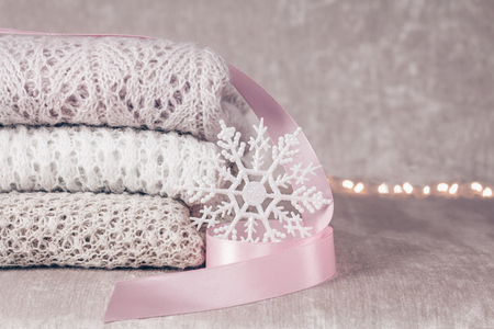 Stylish knitted pastel colored sweaters in different knitting patterns folded in stack with snowflake and pink satin ribbon on velvety fabric background. Close up, copy space.の写真素材