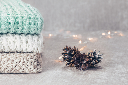 Stylish knitted pastel colored sweaters in different knitting patterns folded in stack with pine cones on velvety fabric background. Winter and spring season knitwear clothing. Close up, copy space.の写真素材