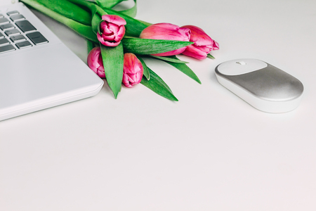 Feminine workspace with white laptop, mouse and bright pink tulip flowers on white table. Spring concept. Copy space.の写真素材