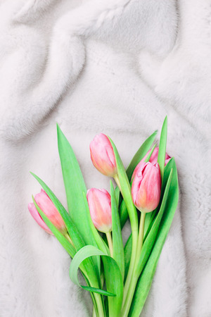 Bouquet of tender pink tulips on silvery white fur background. Winter and spring fur boutique concept. Flat lay. Copy space.の写真素材
