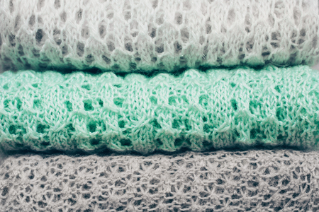 Stylish knitted pastel colored sweaters in different knitting patterns folded in stack. Winter and spring season knitwear clothing with clearly visible texture. Close up, copy space.の写真素材