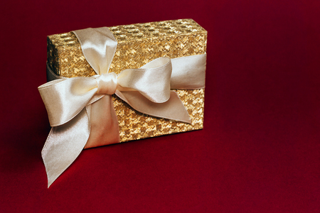 Beautiful shiny golden present box with a silk bow on deep red background. Copy space.の写真素材