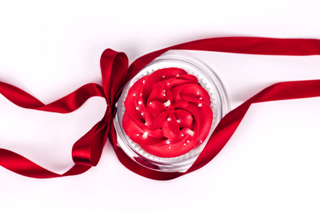 Beautiful cupcake with red icing on the transparent glass plate decorated with silk red curly ribbon with a bow on white background. Text place.の写真素材