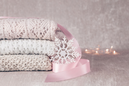 Stylish knitted pastel colored sweaters in different knitting patterns folded in stack with snowflake and pink satin ribbon on velvety fabric background. Close up, copy space.の写真素材