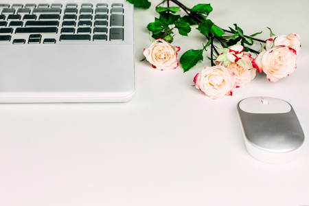 Feminine workspace with white laptop, mouse and beautiful pastel tea roses on white table. Spring concept. Copy space.の写真素材