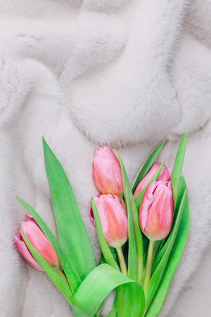 Bouquet of tender pink tulips on silvery white fur background. Winter and spring fur boutique concept. Flat lay. Copy space.の写真素材