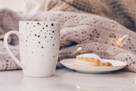 Warm cozy knitwear and a cup of coffee with a cake on white marble windowsill against white window background. Copy space.の写真素材
