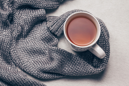 Stylish silvery grey knitted fabric along a cup of tea on milky white fur background. Get over flu concept. Copy space. Top view.の写真素材