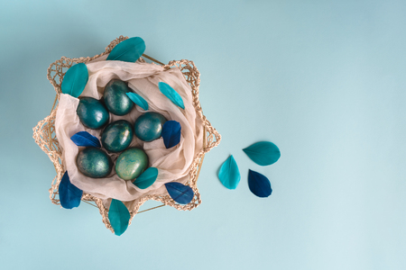 Easter background with eggs decorated in blue, turquoise and gold in nest with colorful blue and turquoise feathers. Top view. Copy space.の写真素材