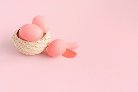 Easter composition made of eggs in basket on pastel pink background decorated with feathers. Greeting card.の写真素材