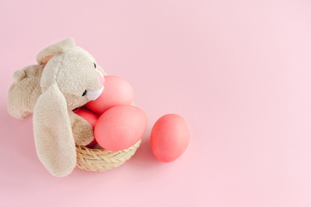 Fluffy Easter rabbit with bright pink colorsd eggs in the basket on pastel rose background. Copy space.の写真素材