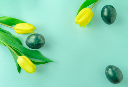 Beautiful spring concept with Easter eggs and yellow tulips on turquiose blue background. Flat lay. Copy space.の写真素材