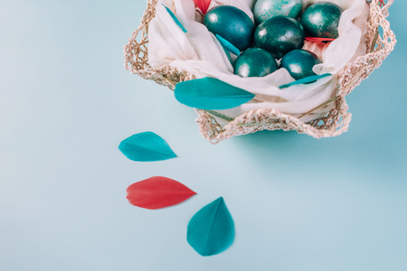 Easter background with eggs decorated in blue, turquoise and gold in nest with colorful coral and turquoise feathers. Close-up. Copy space.の写真素材