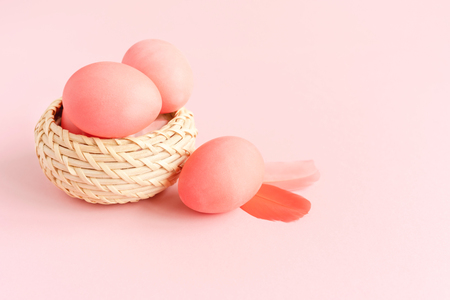 Easter composition made of eggs in the basket on pastel pink background decorated with feathers. Greeting card.の写真素材