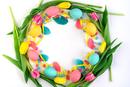 Colorful Easter wreath made of yellow tulips, colorful eggs and candies on white background. Flat lay.の写真素材