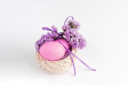 Easter composition made of eggs in basket decorated with flowers in lilac tones on white background. Greeting card. Copy space.の写真素材