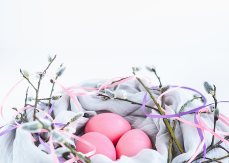 Nest of fabric with pink Easter eggs decorated with silk ribbons and pussy willow on white. Close-up.の写真素材