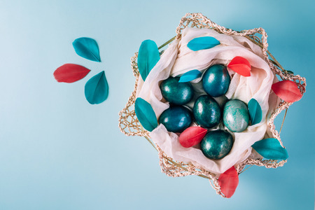 Easter background with eggs decorated in blue, turquoise and gold in nest with colorful coral and turquoise feathers. Top view. Copy space.の写真素材