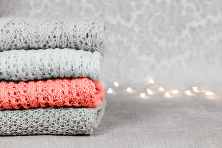 Stylish knitted pastel colored sweaters and one in color of the year 2019 in different knitting patterns folded in stack on velvety fabric background. Winter and spring season knitwear clothing. Close up, copy space.の写真素材