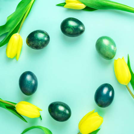 Beautiful spring concept with Easter eggs and yellow tulips in circle on turquiose blue background. Flat lay. Copy space.の写真素材