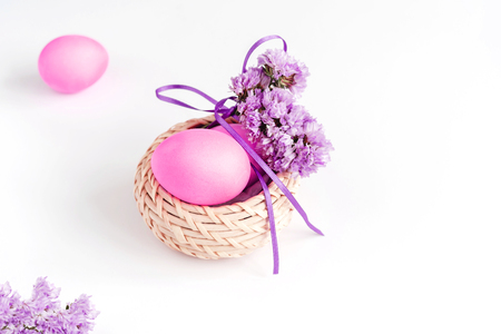 Easter composition made of eggs in basket decorated with flowers in lilac tones on white background. Greeting card. Copy space.の写真素材