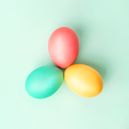 Three colorful handmade Easter eggs in triangle on mint colored background. Flat lay.の写真素材