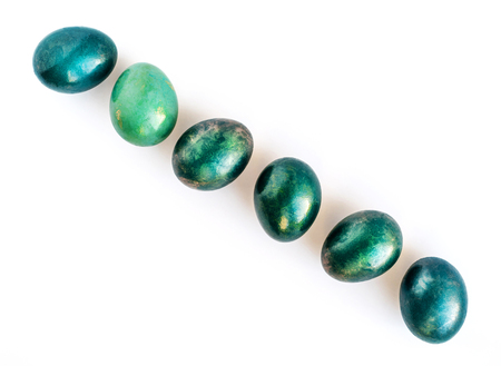 Easter eggs decorated in different shades of turquoise and gold in a diagonal row on white background. Flat lay. Copy space.の写真素材