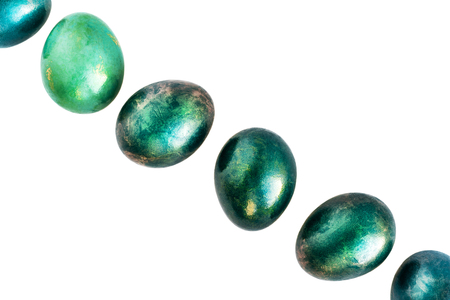 Easter eggs decorated in different shades of turquoise and gold in a diagonal row on white background. Flat lay. Close-up.の写真素材